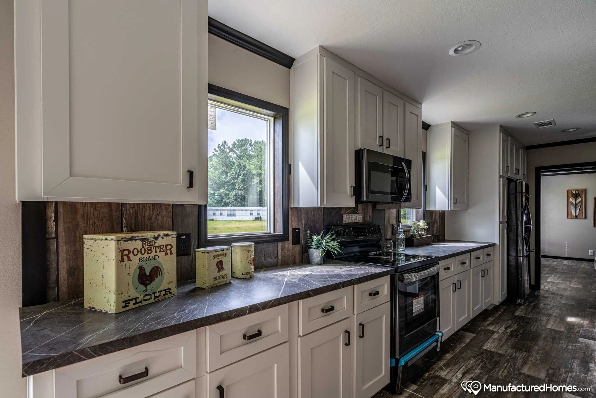 A kitchen with white cabinets , black appliances , and a window.