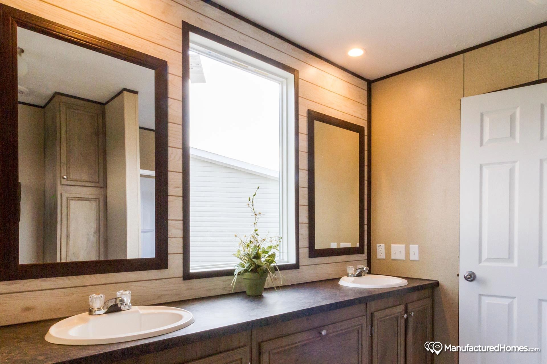 A bathroom with two sinks , two mirrors and a window.