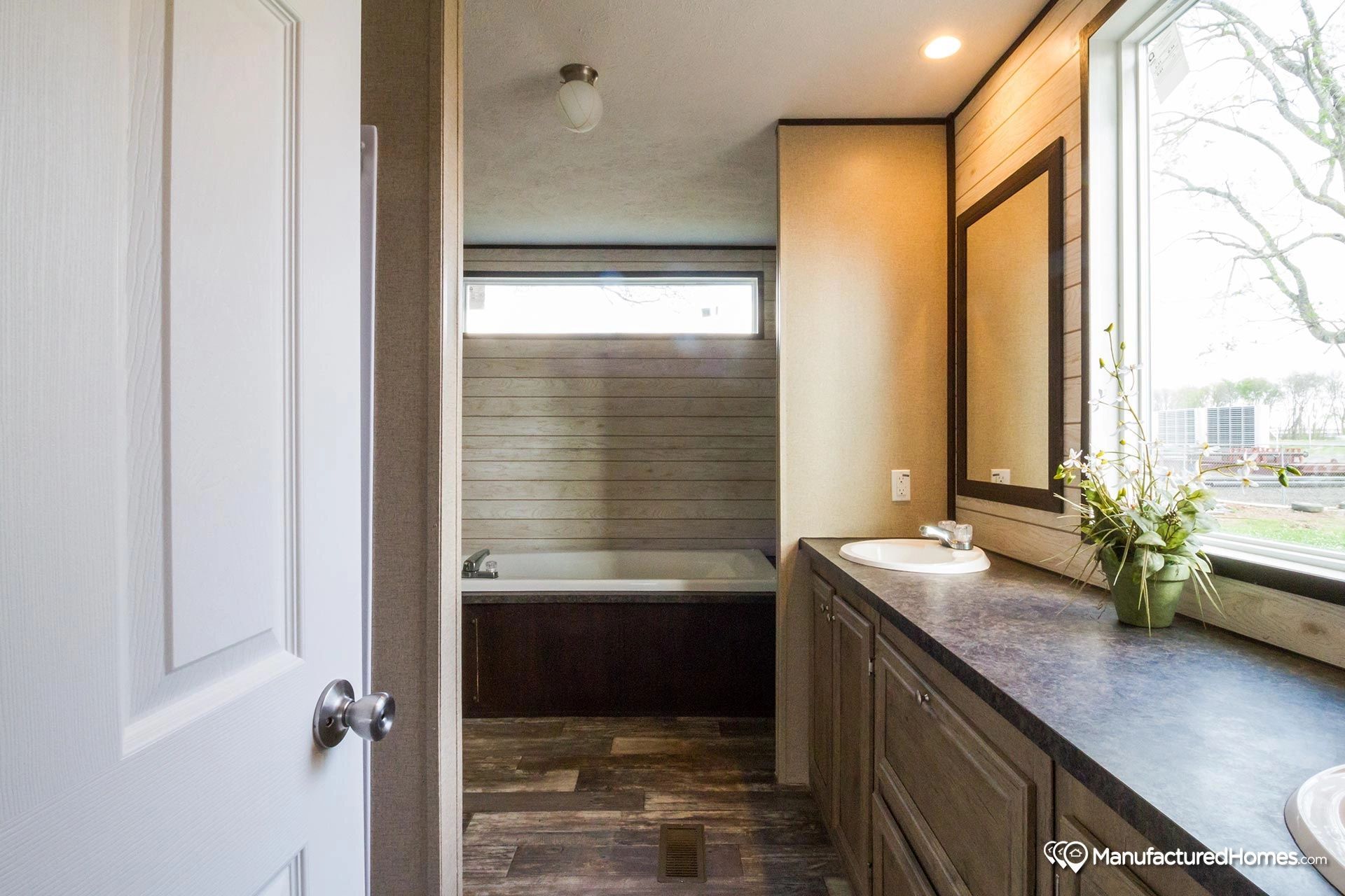 A bathroom with a tub , sink , mirror and window.