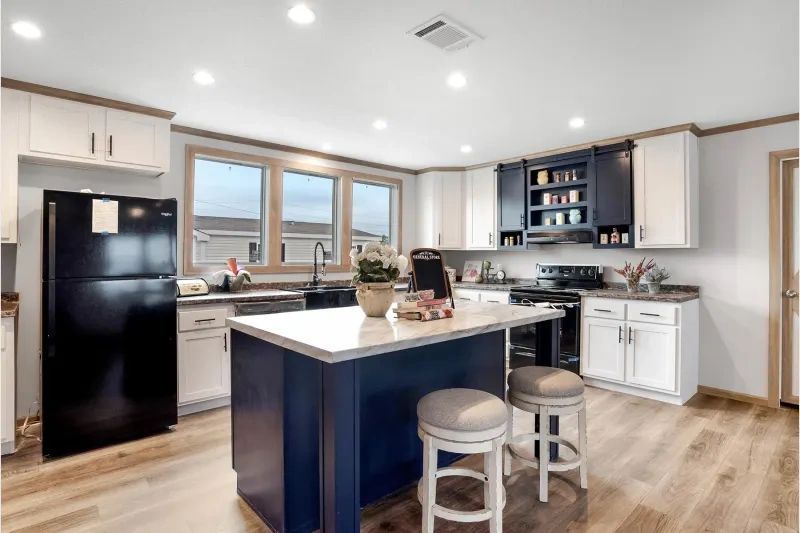 A kitchen with a blue island , white cabinets , a black refrigerator , and stools.