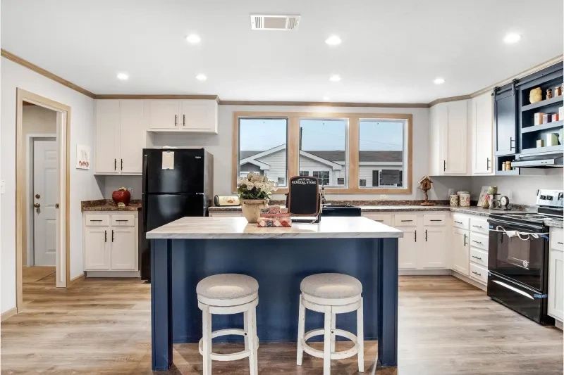 A kitchen with a blue island , white cabinets , a black refrigerator , and a stove.