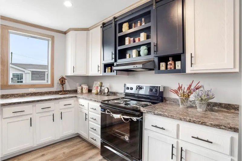 A kitchen with white cabinets , black appliances , granite counter tops and a window.