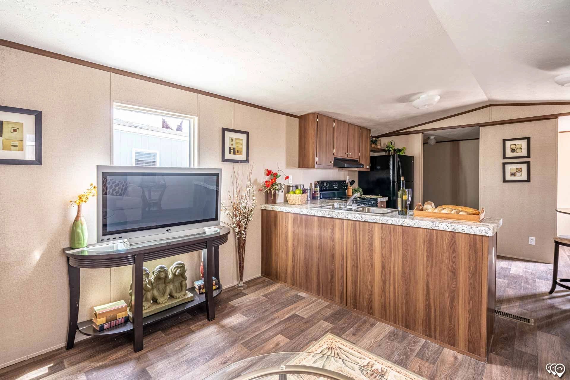 A living room with a television and a kitchen in a mobile home.