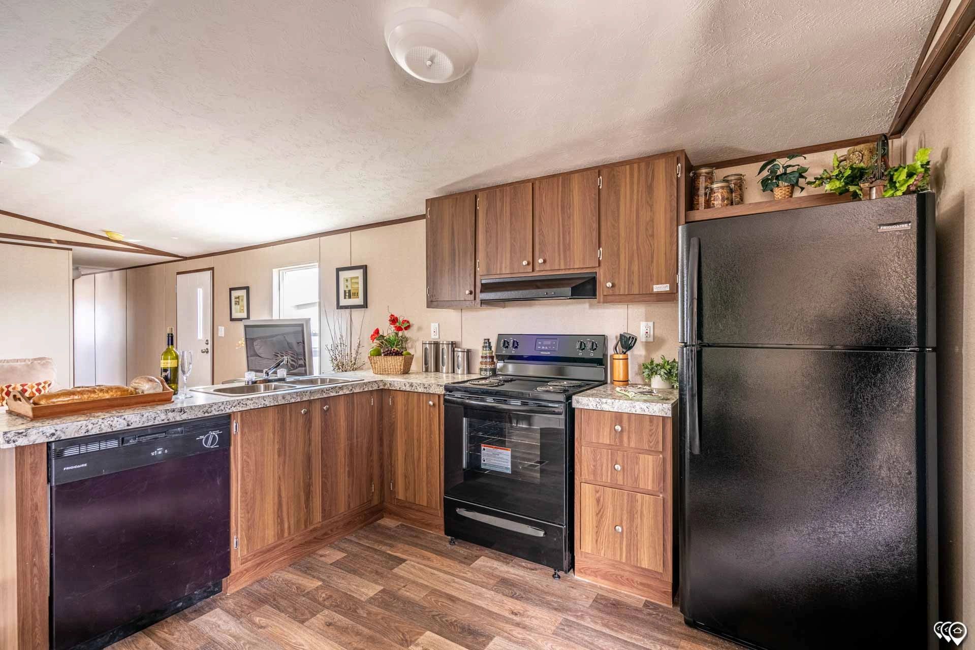 A kitchen in a mobile home with a black refrigerator , stove , and dishwasher.