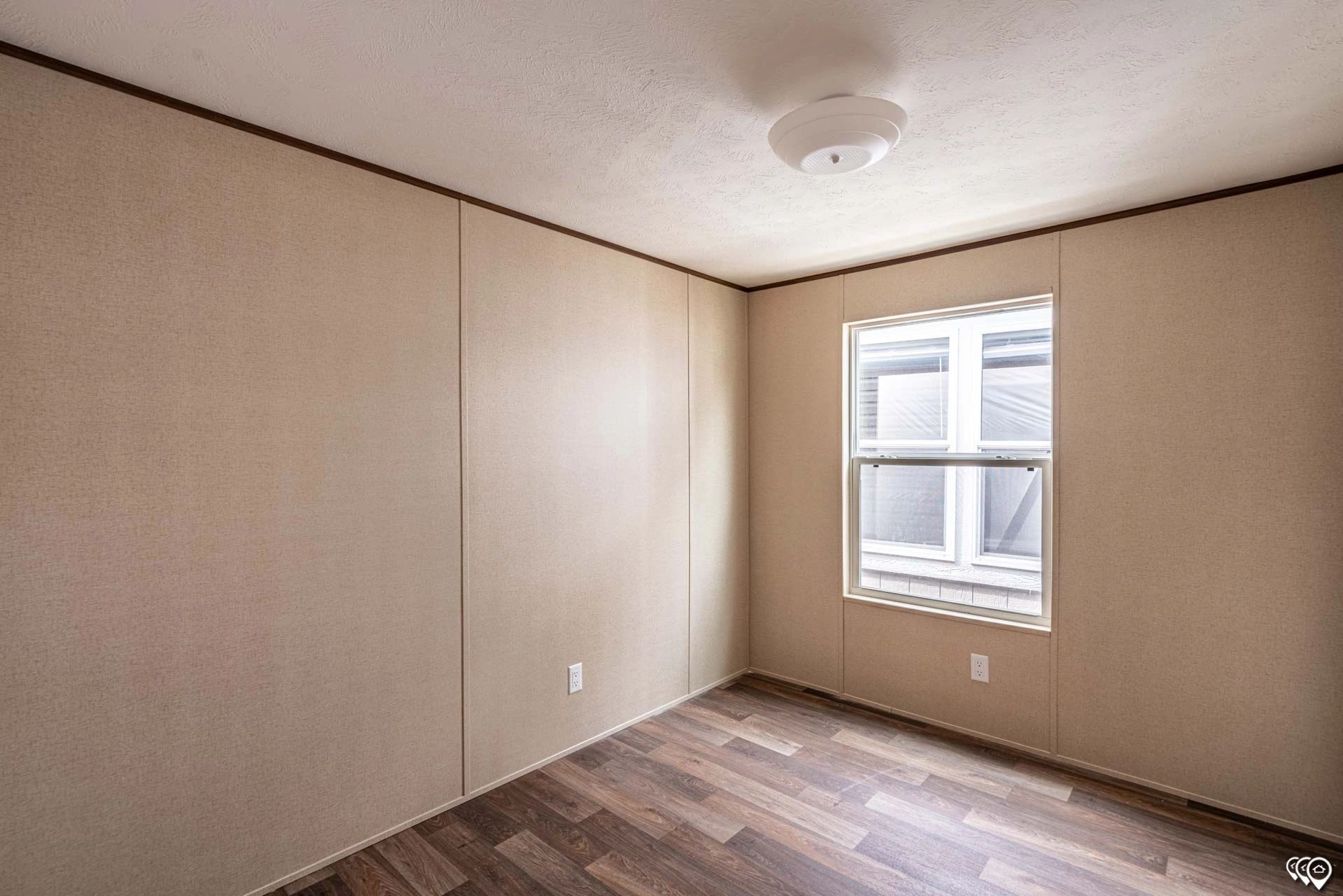 An empty room with a window and wooden floors in a mobile home.