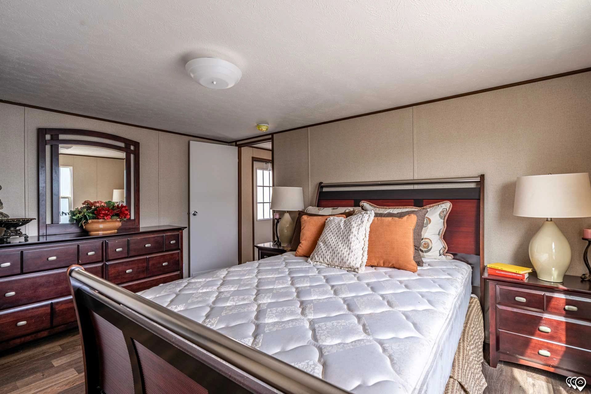 A bedroom with a bed , dresser , nightstand , mirror and lamps.