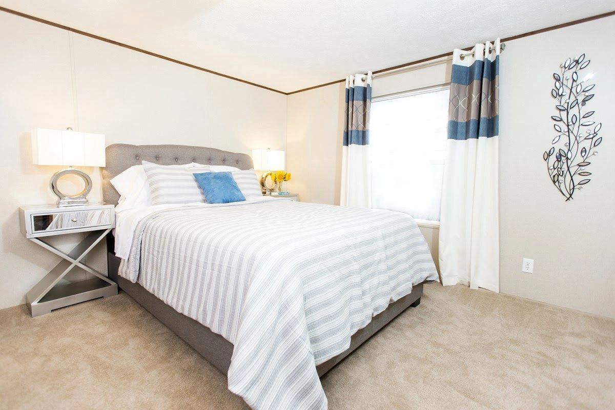 A bedroom with a bed , nightstand , lamps and curtains.