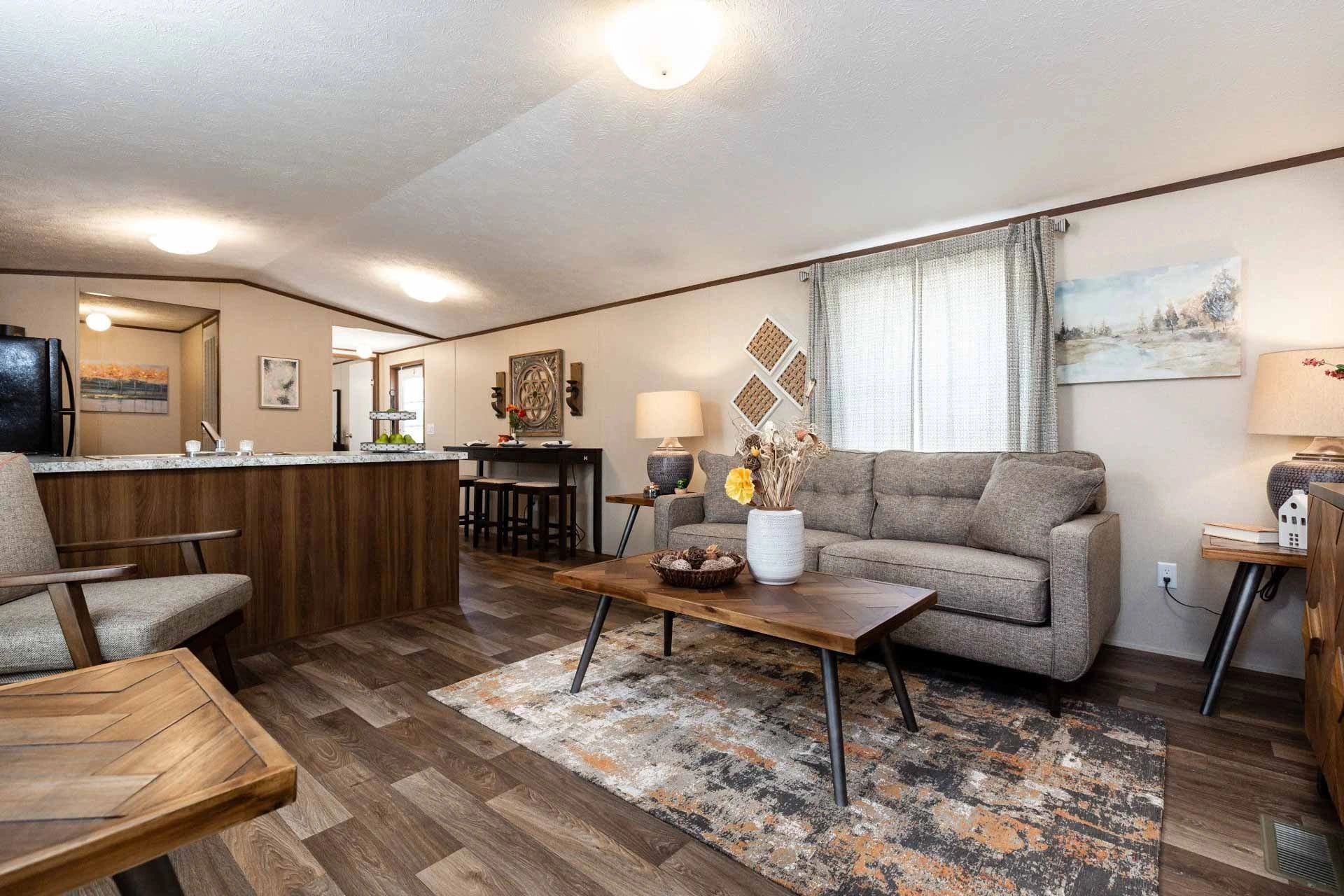 A living room in a mobile home with a couch , chair , coffee table and rug.