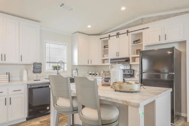 A kitchen with white cabinets , stainless steel appliances , a refrigerator and a table with two chairs.