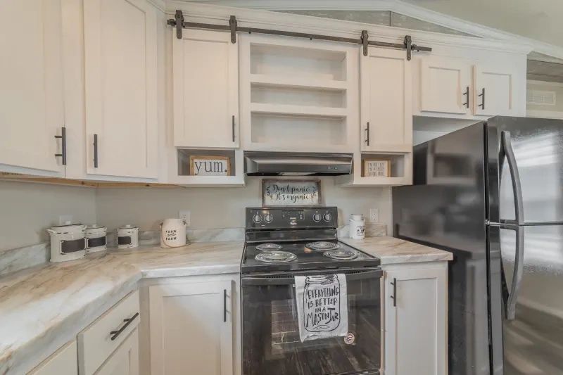 A kitchen with white cabinets , a stove , a refrigerator and a microwave.