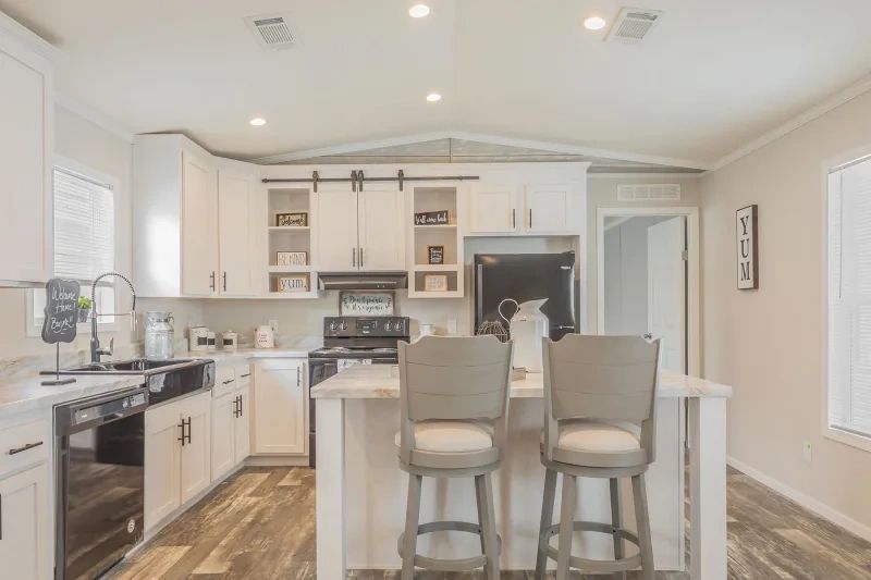 A kitchen in a mobile home with white cabinets and stools.