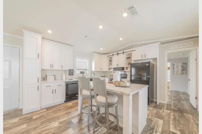 A kitchen in a mobile home with white cabinets and wooden floors.