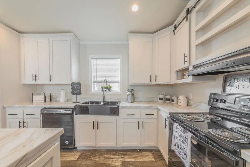 A kitchen with white cabinets , a stove , a sink , and a window.