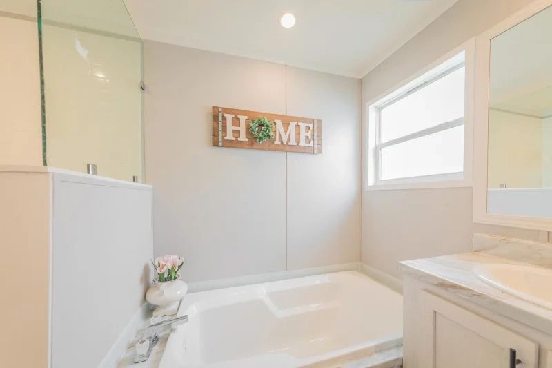 A bathroom with a tub , sink , mirror and a sign on the wall that says `` home ''.