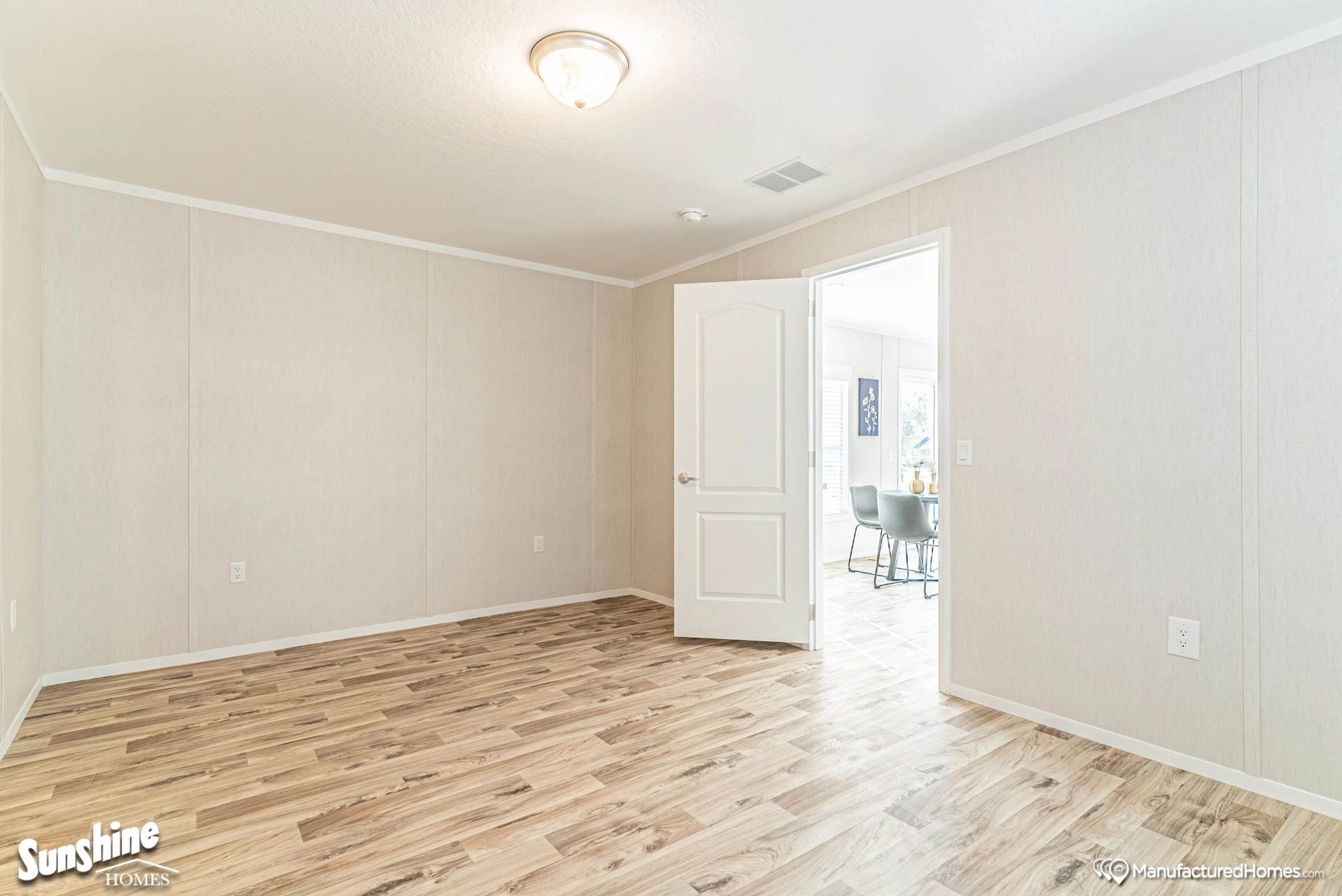 An empty room with hardwood floors and a door leading to a dining room.