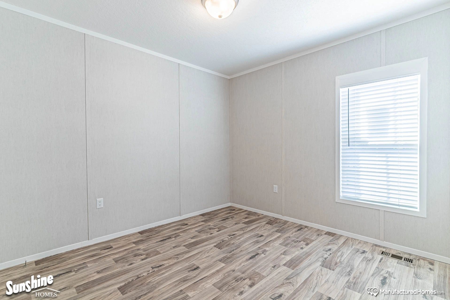 A bedroom in a mobile home with hardwood floors and a window.