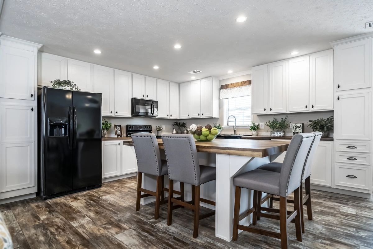 A kitchen with white cabinets , a black refrigerator , a table and chairs.