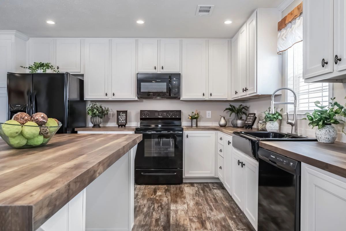 A kitchen with white cabinets , black appliances , and a wooden counter top.