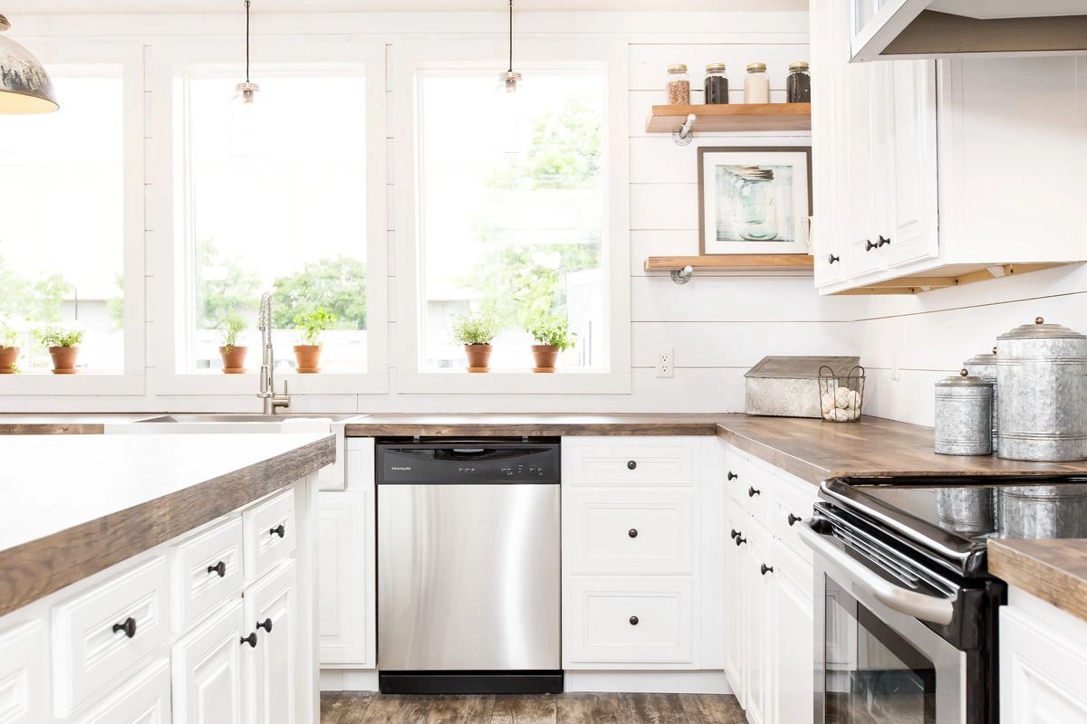 A kitchen with white cabinets , a stainless steel dishwasher , a stove , and a sink.