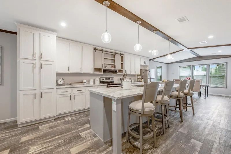 A kitchen with white cabinets , a large island , a dining table and chairs.