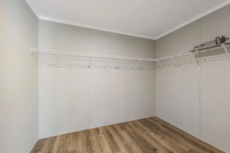 An empty walk in closet with hardwood floors and white shelves.