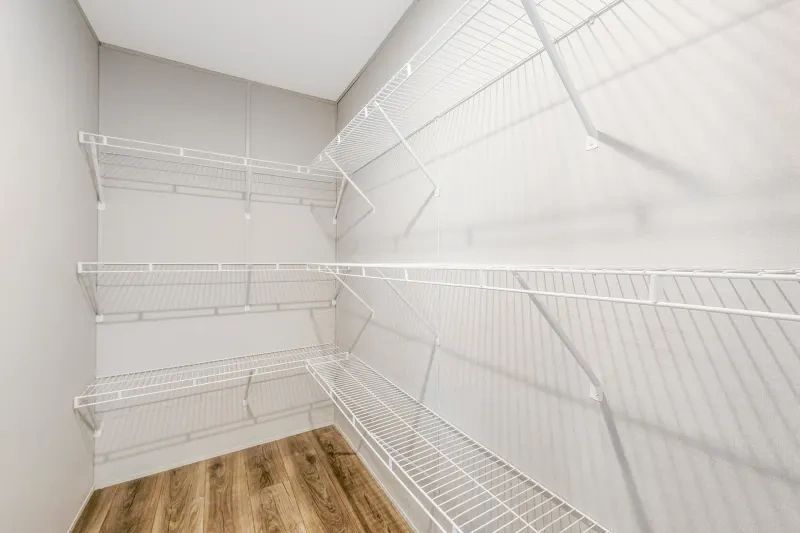A walk in closet with wooden floors and white wire shelves.