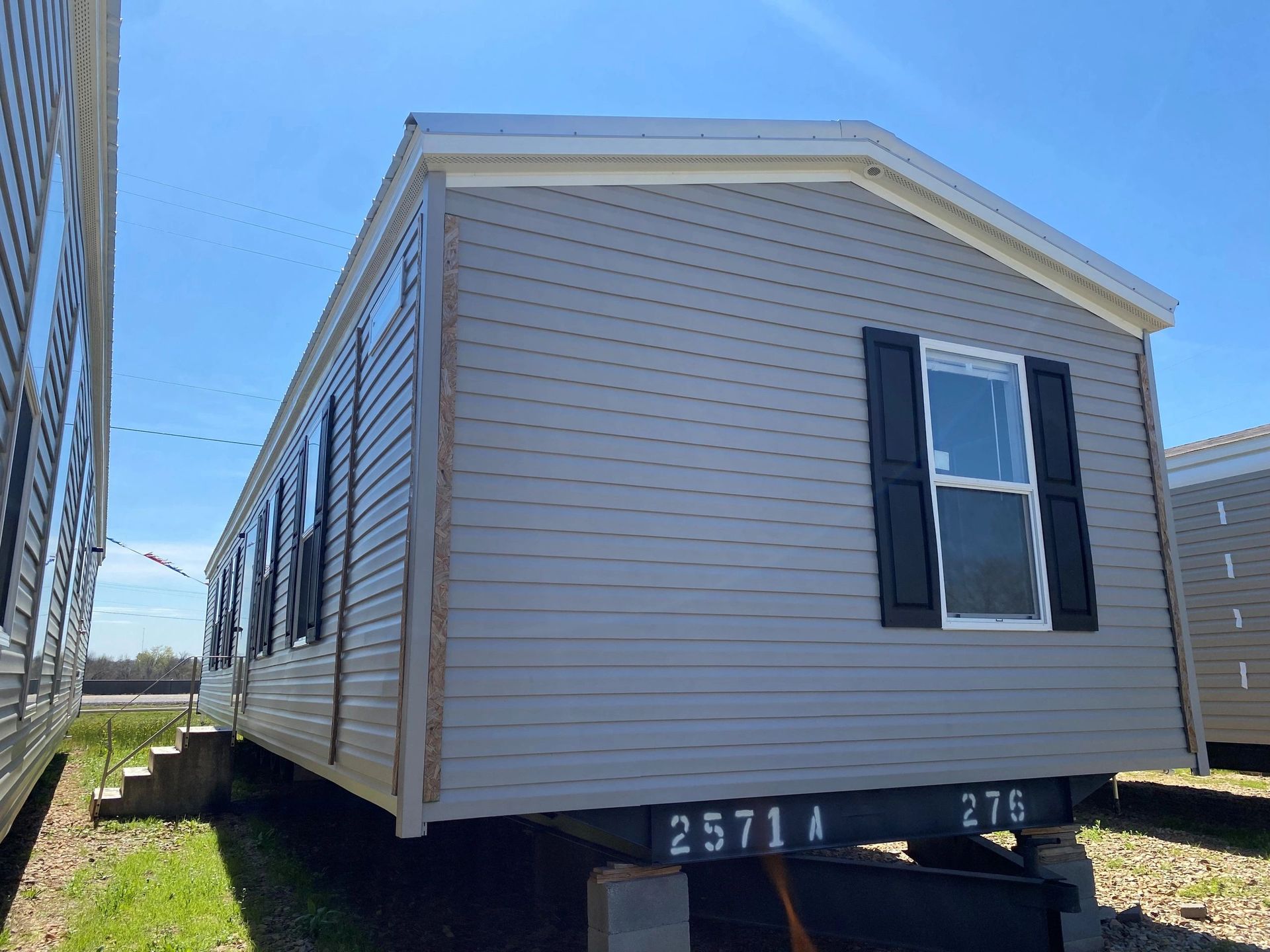 A mobile home with black shutters is parked in a field.