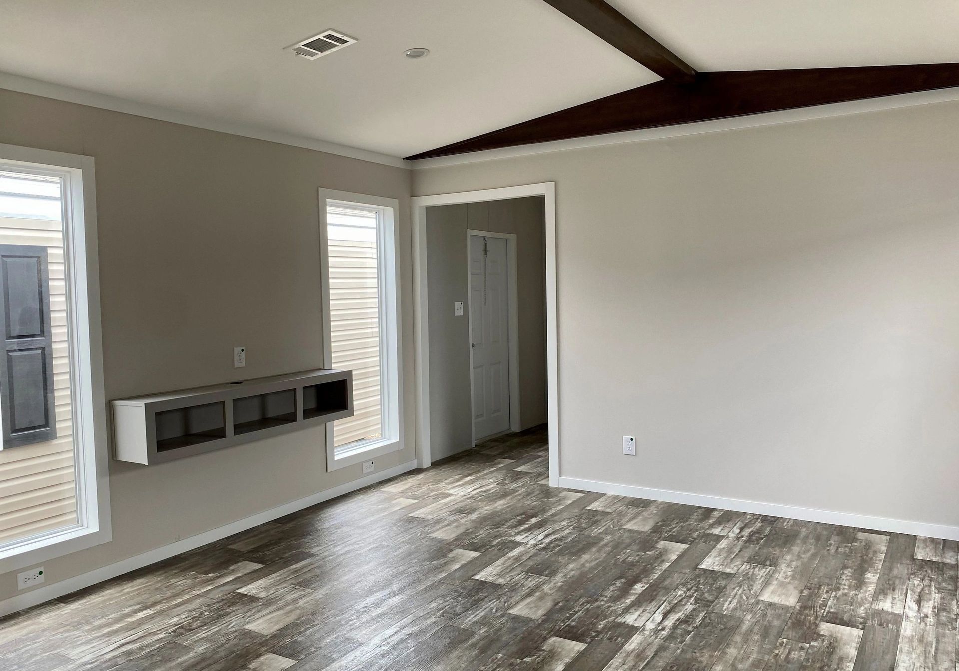 An empty living room in a mobile home with hardwood floors and white walls.