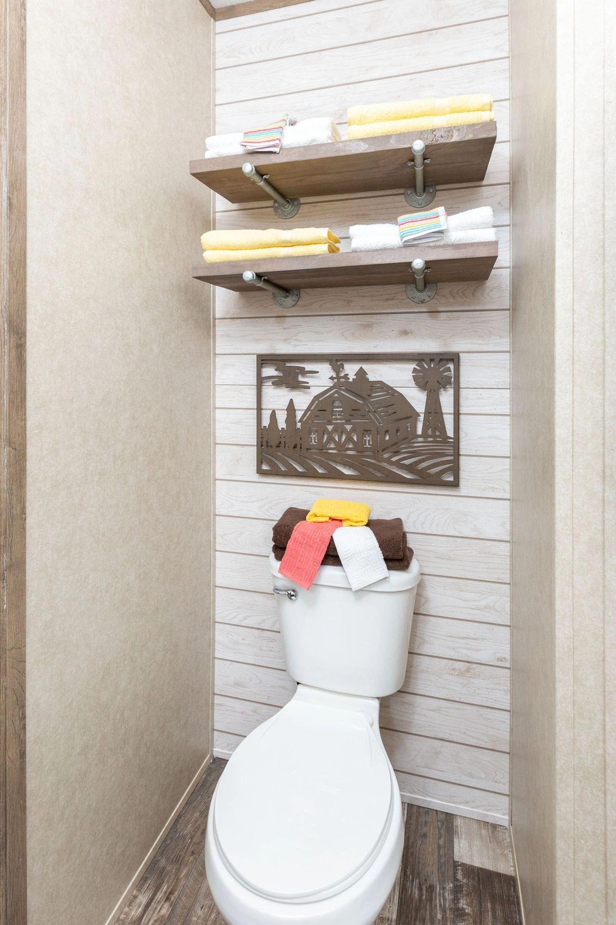 A bathroom with a toilet , shelves and a picture on the wall.