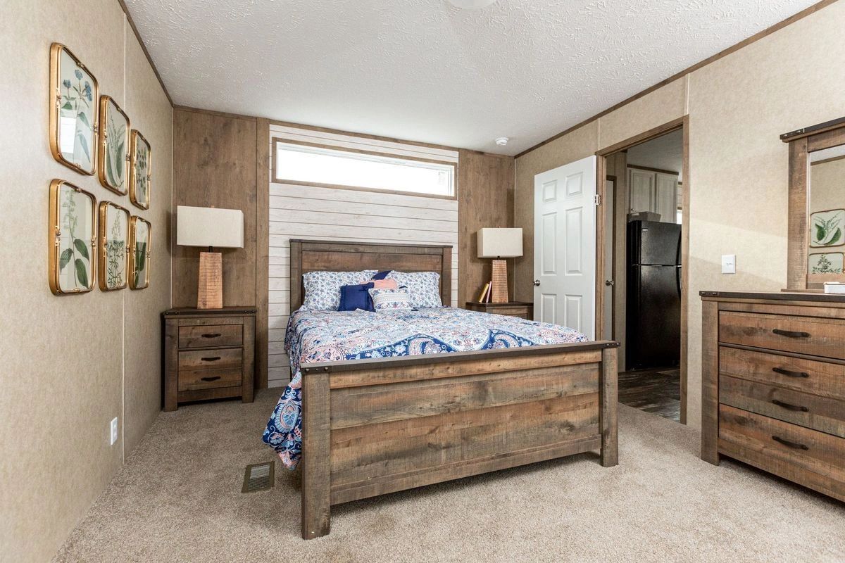 A bedroom with a bed , dresser , nightstand and mirror.