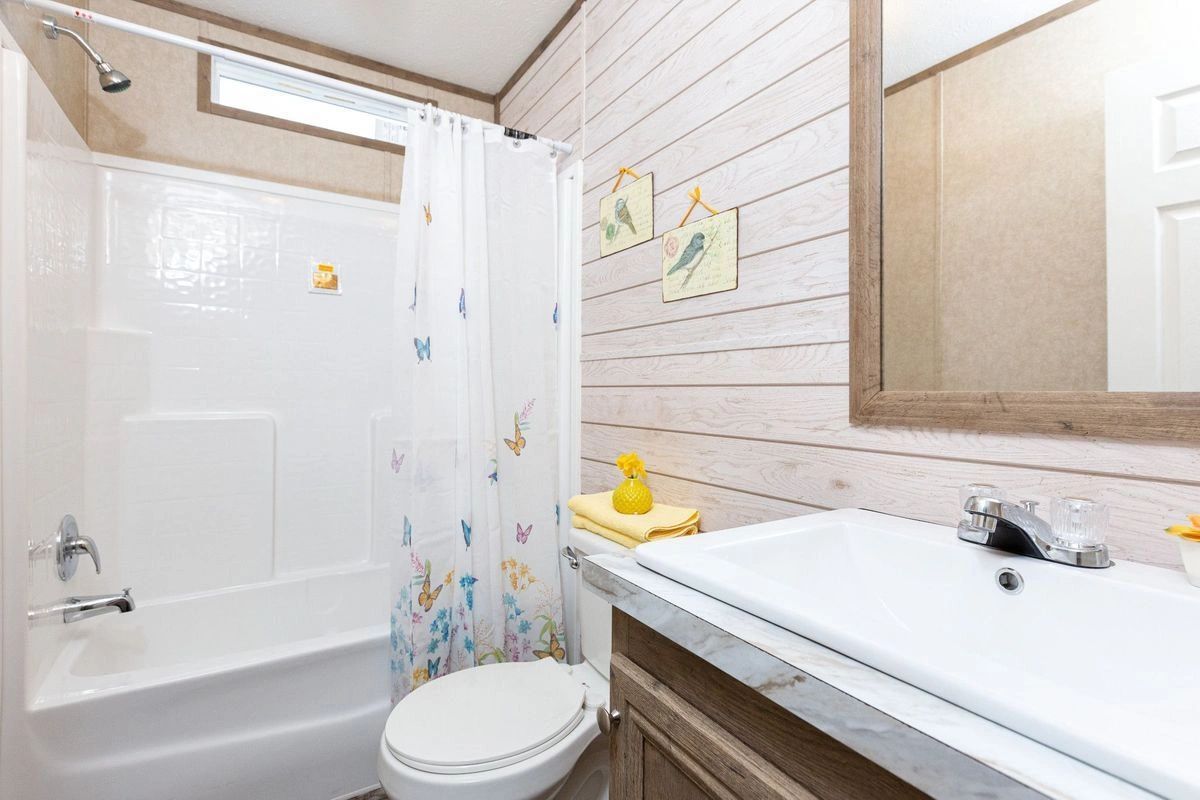 A bathroom with a toilet , sink , shower and mirror.