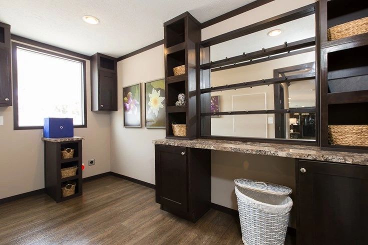 A room with a desk , shelves , a mirror and a trash can.