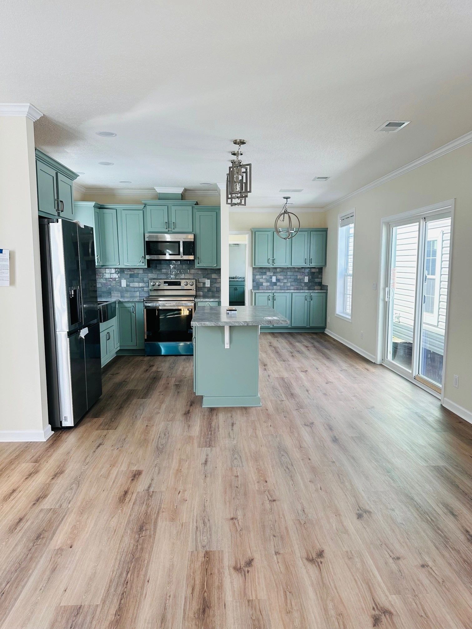 A kitchen with blue cabinets , a black refrigerator , and a wooden floor.
