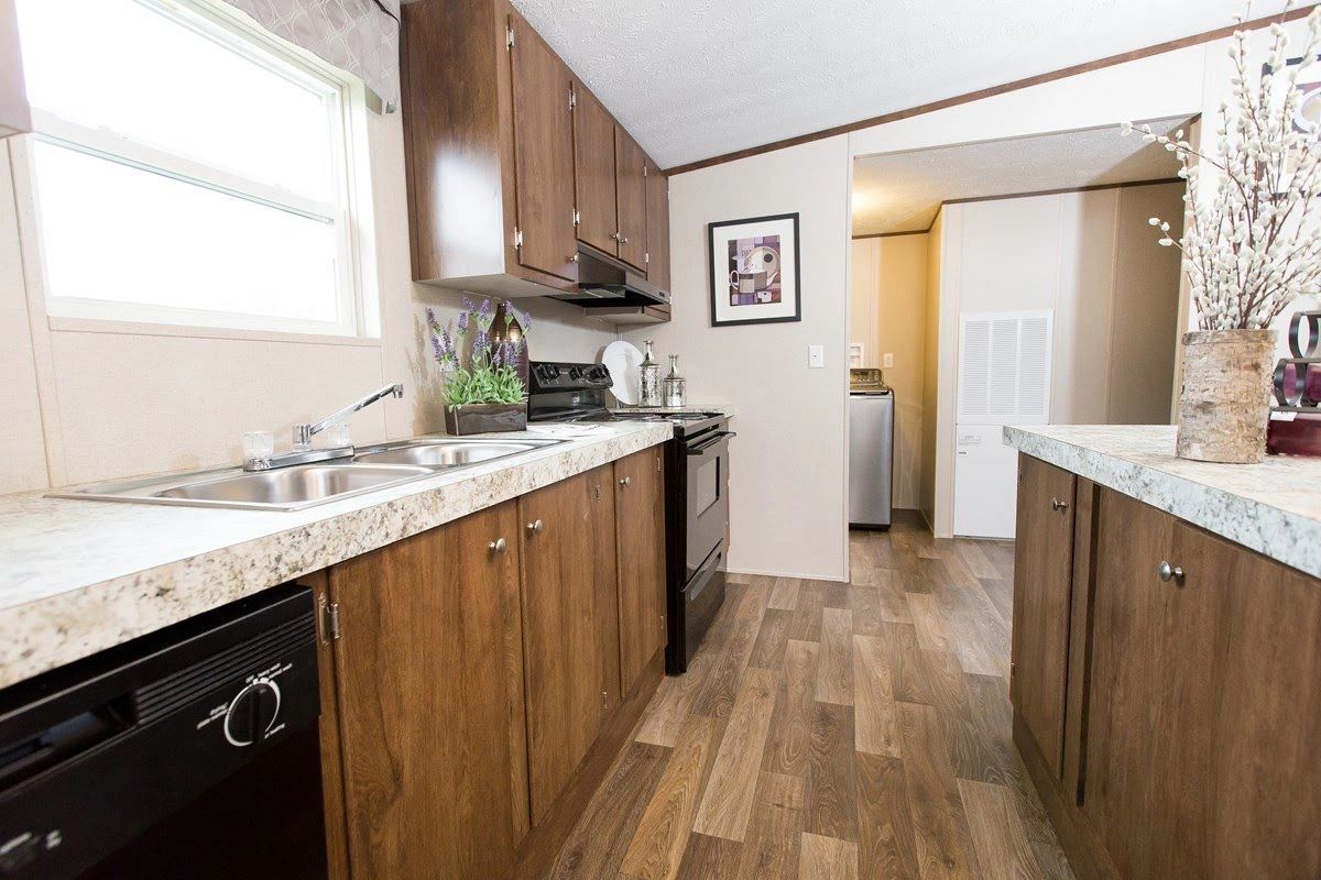 A kitchen in a mobile home with wooden cabinets and a black dishwasher.