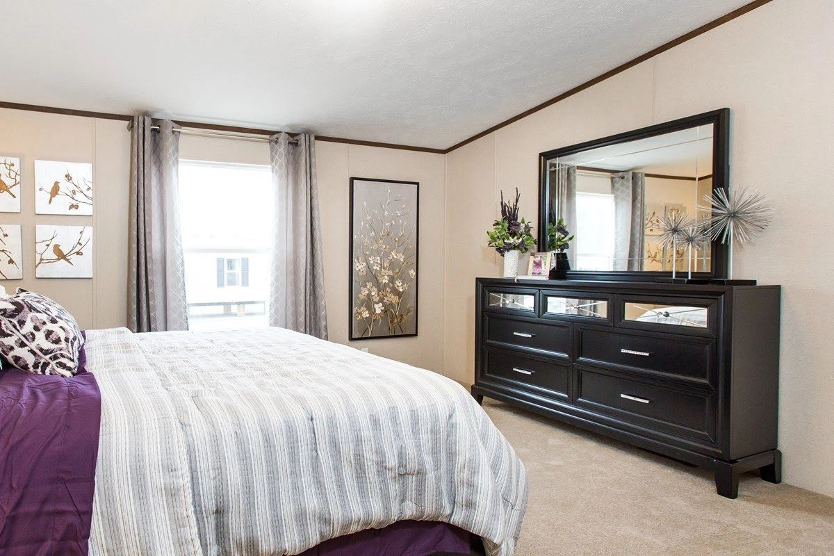 A bedroom with a bed , dresser , mirror and window.