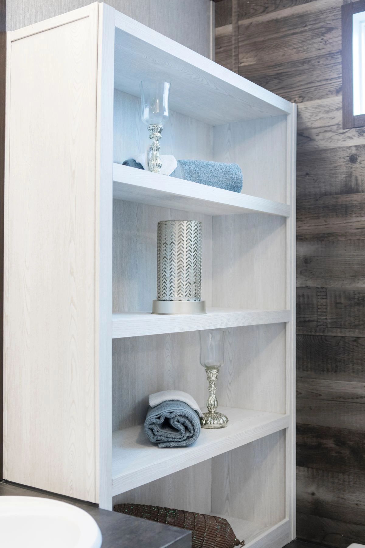 A bathroom with a white bookshelf filled with towels and candles.