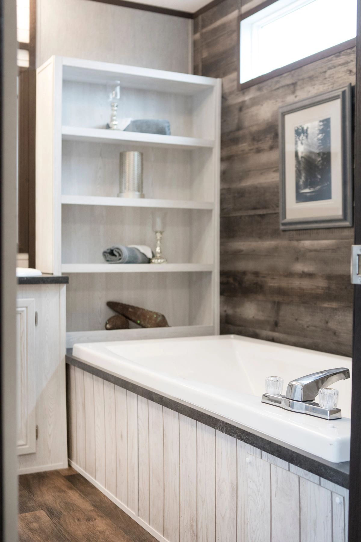 A bathroom with a bathtub , shelves , and a picture on the wall.