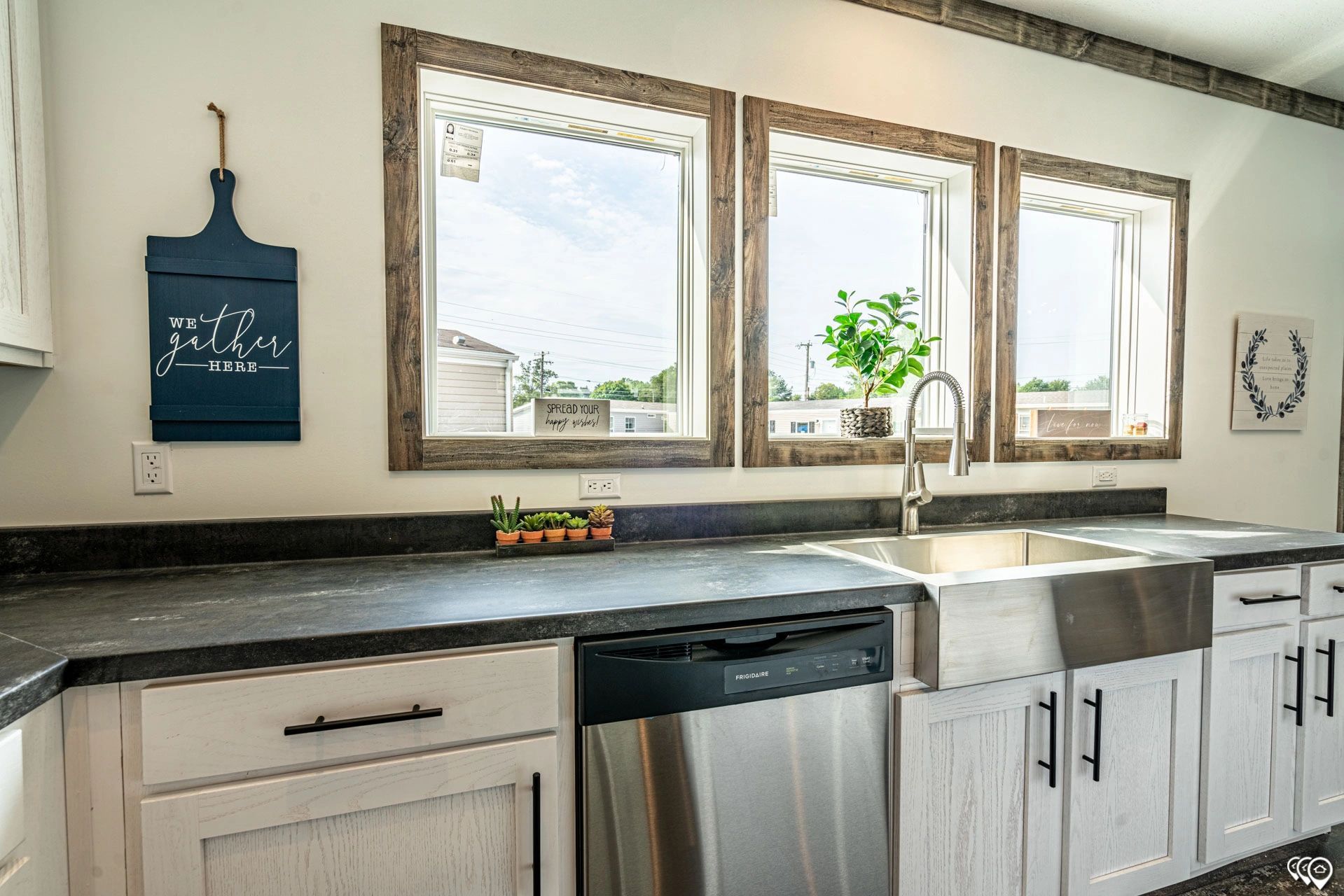 A kitchen with a sink , dishwasher , and three windows.