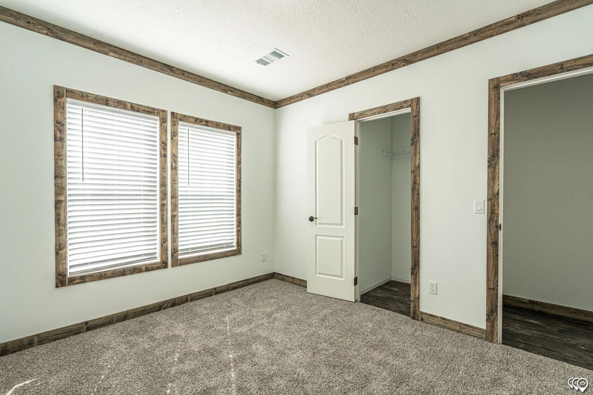 An empty bedroom with two windows and a walk in closet.