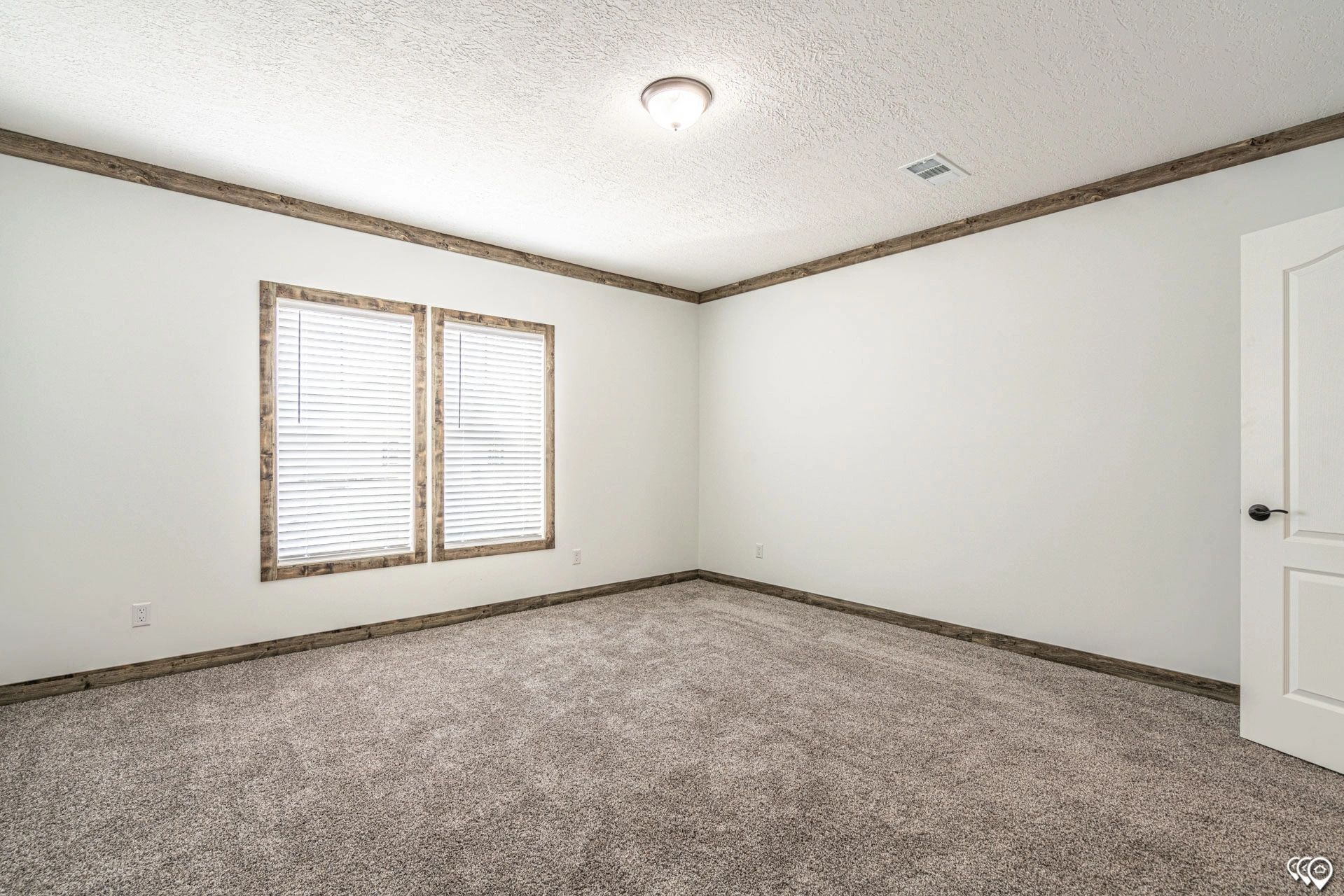 An empty bedroom with a carpeted floor and two windows.