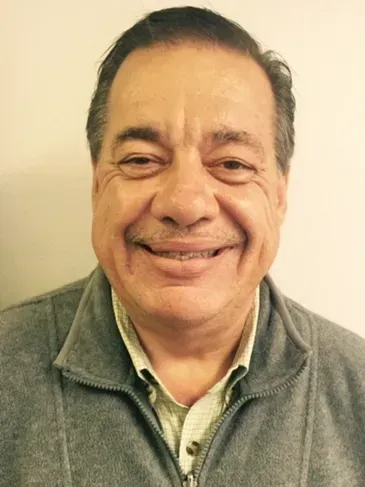 A man with a mustache is smiling for the camera while wearing a gray jacket.