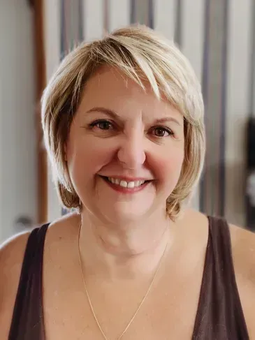 A woman wearing a brown tank top and a necklace is smiling for the camera.