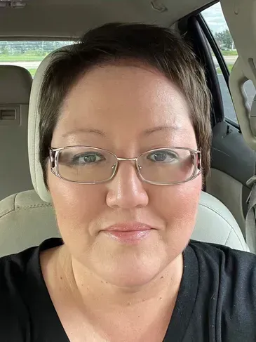 A woman wearing glasses is sitting in the back seat of a car.