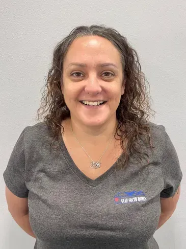 A woman wearing a gray shirt and a necklace is smiling for the camera.