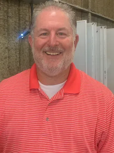 A man with a beard is wearing a red striped shirt and smiling.