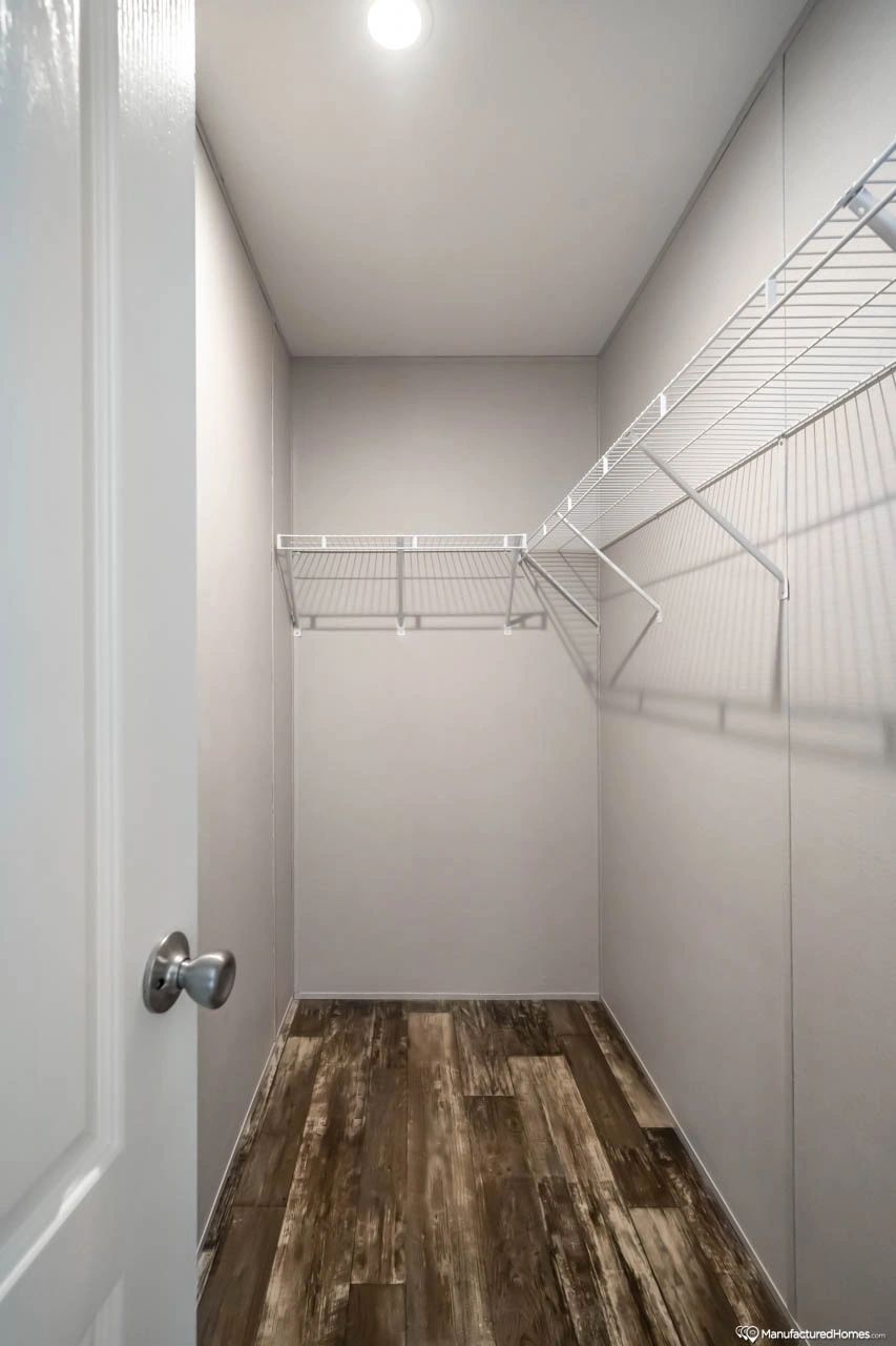 A walk in closet with wooden floors and white wire shelves.