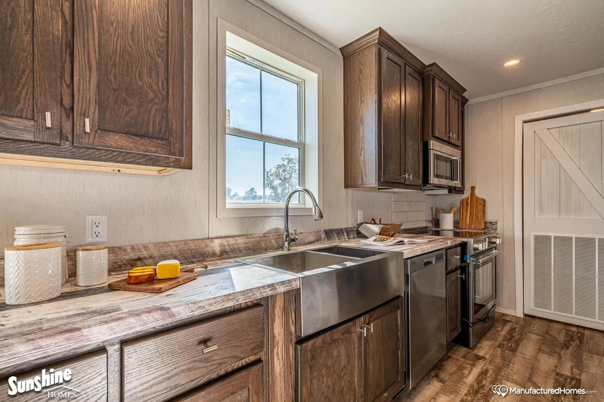 A kitchen with stainless steel appliances , wooden cabinets , a sink and a window.