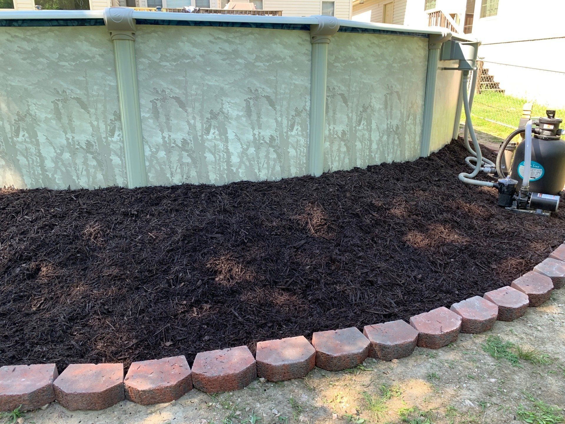 A swimming pool is surrounded by mulch and bricks.