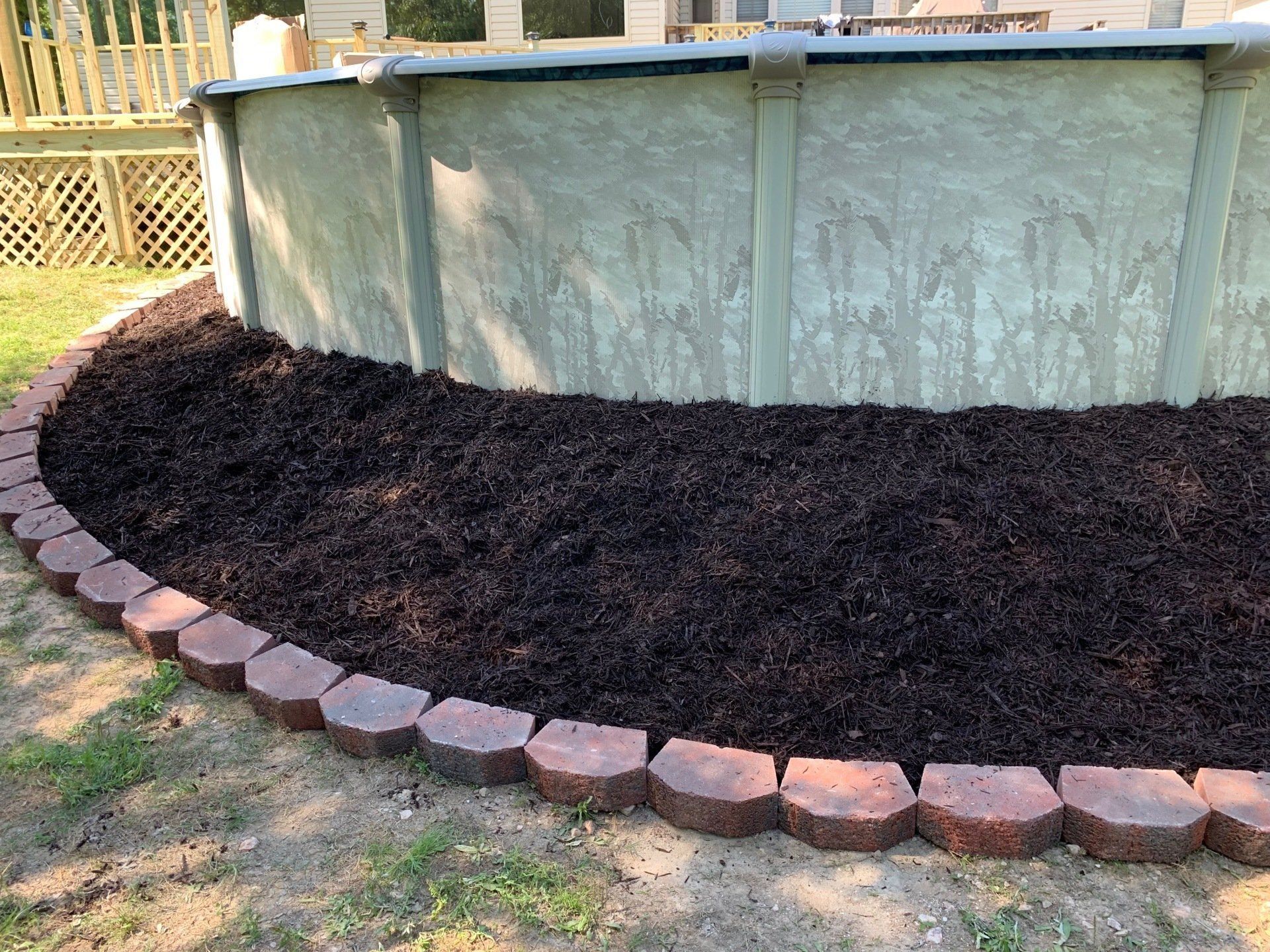 A swimming pool is surrounded by mulch and bricks in a backyard.