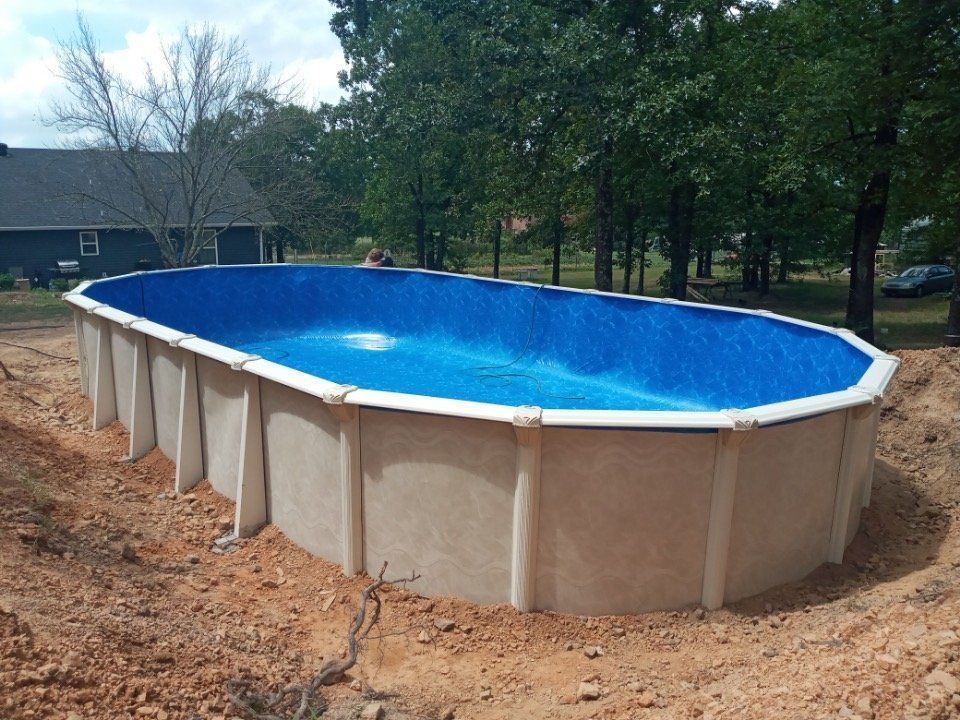 A large swimming pool is sitting in the dirt in front of a house